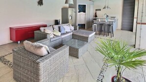 A modern living area with wicker furniture, a red cabinet, and a kitchen in the background.