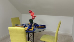 Un comedor con una mesa redonda de vidrio, sillas amarillas y una pequeña maceta con flores rojas.