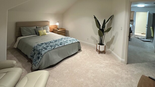 Un dormitorio con cama, mesitas de noche, una planta en maceta y vista a otra habitación.