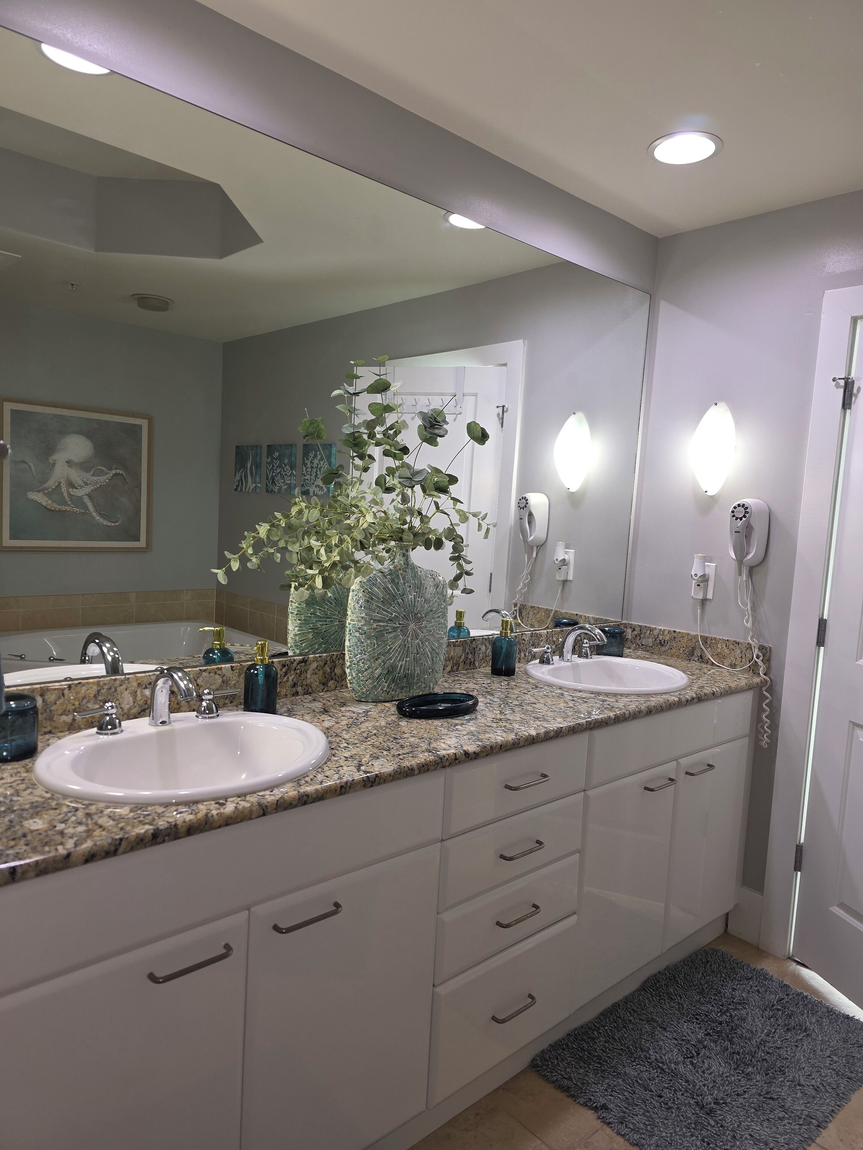 A modern bathroom with two sinks, a large mirror, and a potted plant.