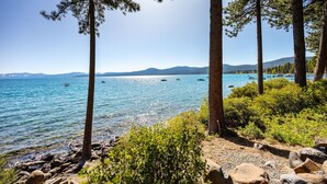 A clear view of a lake with boats, surrounded by trees and rocky terrain. - Remodeled 4BR Lakefront w/ Exceptional Amenities (Kings Beach)