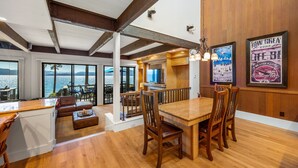A spacious living area with a wooden dining table and chairs, a sofa, and a kitchen area with a large window overlooking a scenic view. - Remodeled 4BR Lakefront w/ Exceptional Amenities (Kings Beach)
