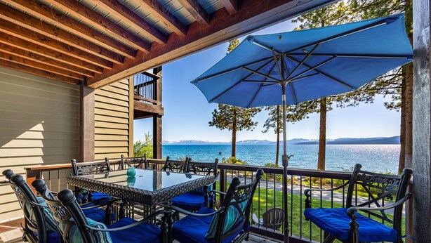A covered outdoor seating area with a table and chairs, overlooking a body of water. - Remodeled 4BR Lakefront w/ Exceptional Amenities (Kings Beach)