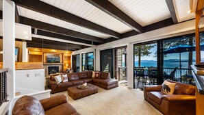 A spacious living room with a large sectional sofa, a fireplace, and a view of the outdoors. - Remodeled 4BR Lakefront w/ Exceptional Amenities (Kings Beach)