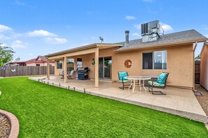 Une maison avec un patio, un barbecue et un espace couvert comprenant des chaises et une table.