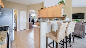 Una cocina moderna con una isla central, taburetes de bar, un refrigerador y un televisor.