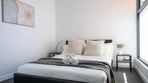Un lit bien fait, avec des serviettes pliées, une table de chevet avec une lampe et une œuvre d’art accrochée au mur.