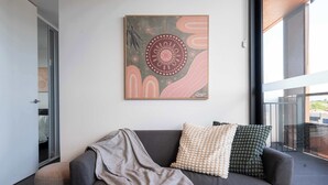 Un salon moderne avec un canapé gris, une couverture et des coussins à motifs. Un grand tableau abstrait est accroché au mur.