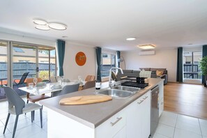 A modern kitchen with a central island, a dining area with chairs, a sofa, and a view of the outside.