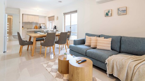 Ein modernes Wohnzimmer mit grauem Sofa, Holztisch und einem Essbereich mit Stühlen und Tisch.