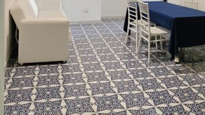 Una habitación con piso estampado, un sofá blanco, una mesa de comedor con sillas y una lámpara colgante.