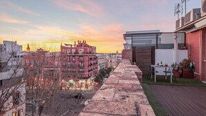 Terraza en la azotea con vista panorámica del paisaje urbano al atardecer, que incluye un camino de piedra, una pequeña mesa con sillas y plantas en macetas.