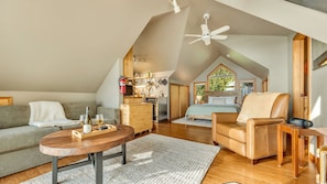 A cozy loft bedroom with a sloped ceiling, a wooden desk, a sofa, and a chair. - Neahkahnie Nest by Manzanita Beach Getaway: Luxury Studio, Ocean Views, Hot Tub (Nehalem)
