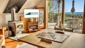 Una habitación acogedora con estufa de leña, televisión, una mesa con fichas de Scrabble y vista al mar.