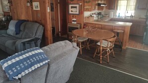 A cozy living room with a grey sofa, a blue patterned throw, and a wooden dining table with chairs. - Catfish Cove at Watts bar Lake (Rockwood)