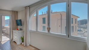 Een kamer met een groot rondboogvenster, een witte dressoir, een klein tafeltje en een potplant.