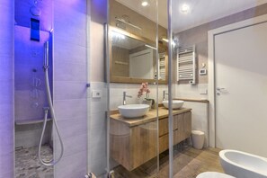 Ein modernes Badezimmer mit Duschkabine aus Glas, zwei Waschbecken, einem großen Spiegel und einer Toilette.