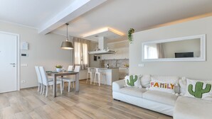 Een moderne woonkamer met een bank, eettafel en stoelen. Er is een keuken met een spoelbak en kasten.
