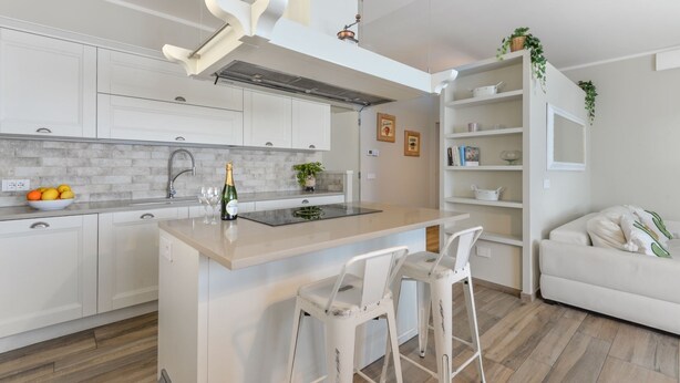Een moderne keuken met witte kasten, een marmeren aanrechtblad en een centraal eiland met barstoelen.
