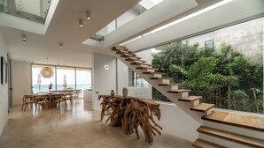 Un intérieur moderne avec un escalier, un coin repas et de grandes fenêtres donnant sur un espace verdoyant.