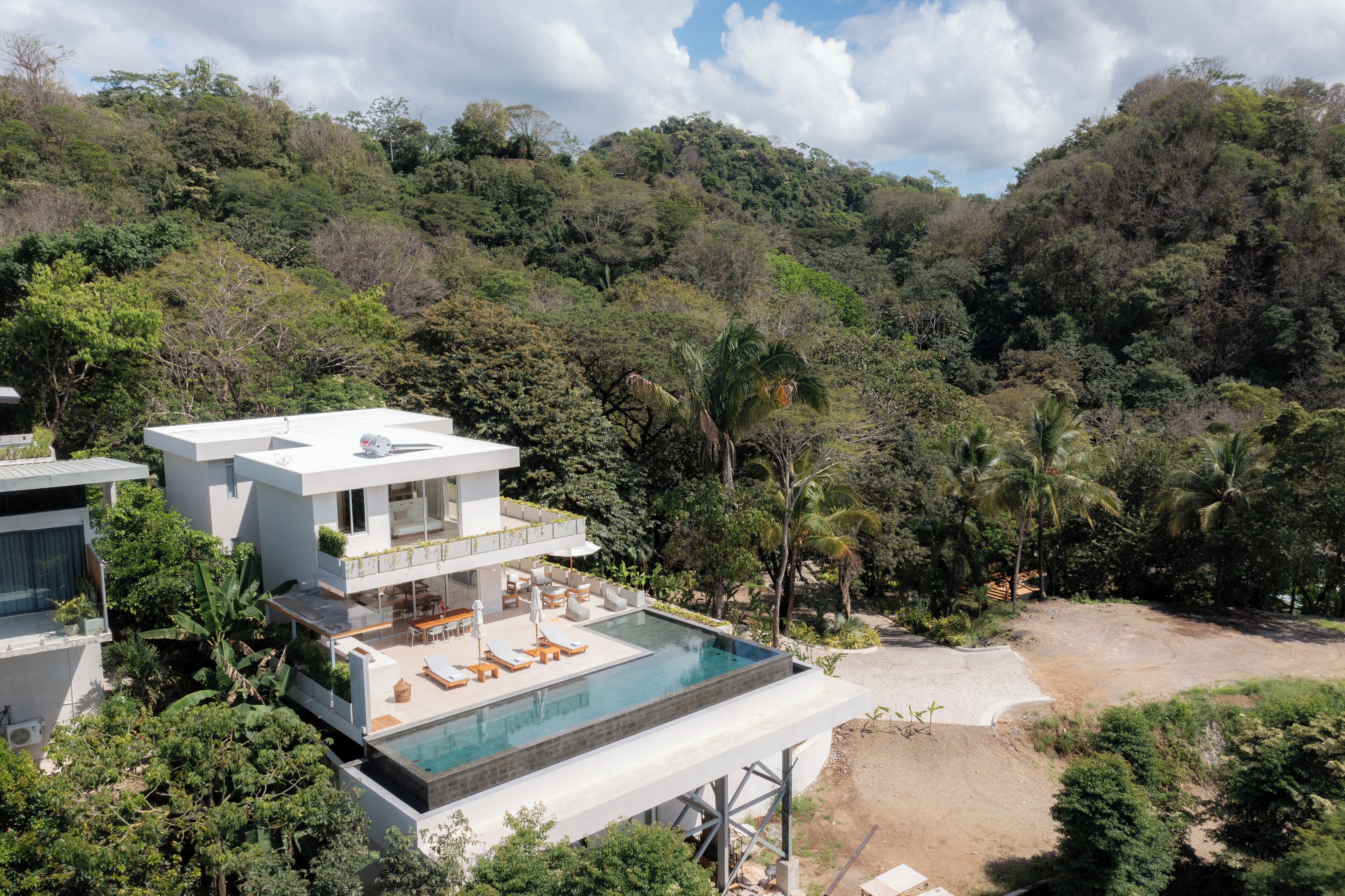 A modern house with a pool, surrounded by lush greenery and hills.