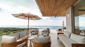 Un espace extérieur moderne, aménagé avec du mobilier en bois et doté d’un grand parasol, offrant une vue imprenable sur l’océan.