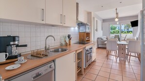 Eine moderne Küche mit Geschirrspüler, Backofen und Kaffeemaschine. Es gibt einen Essbereich mit Tisch und Stühlen.