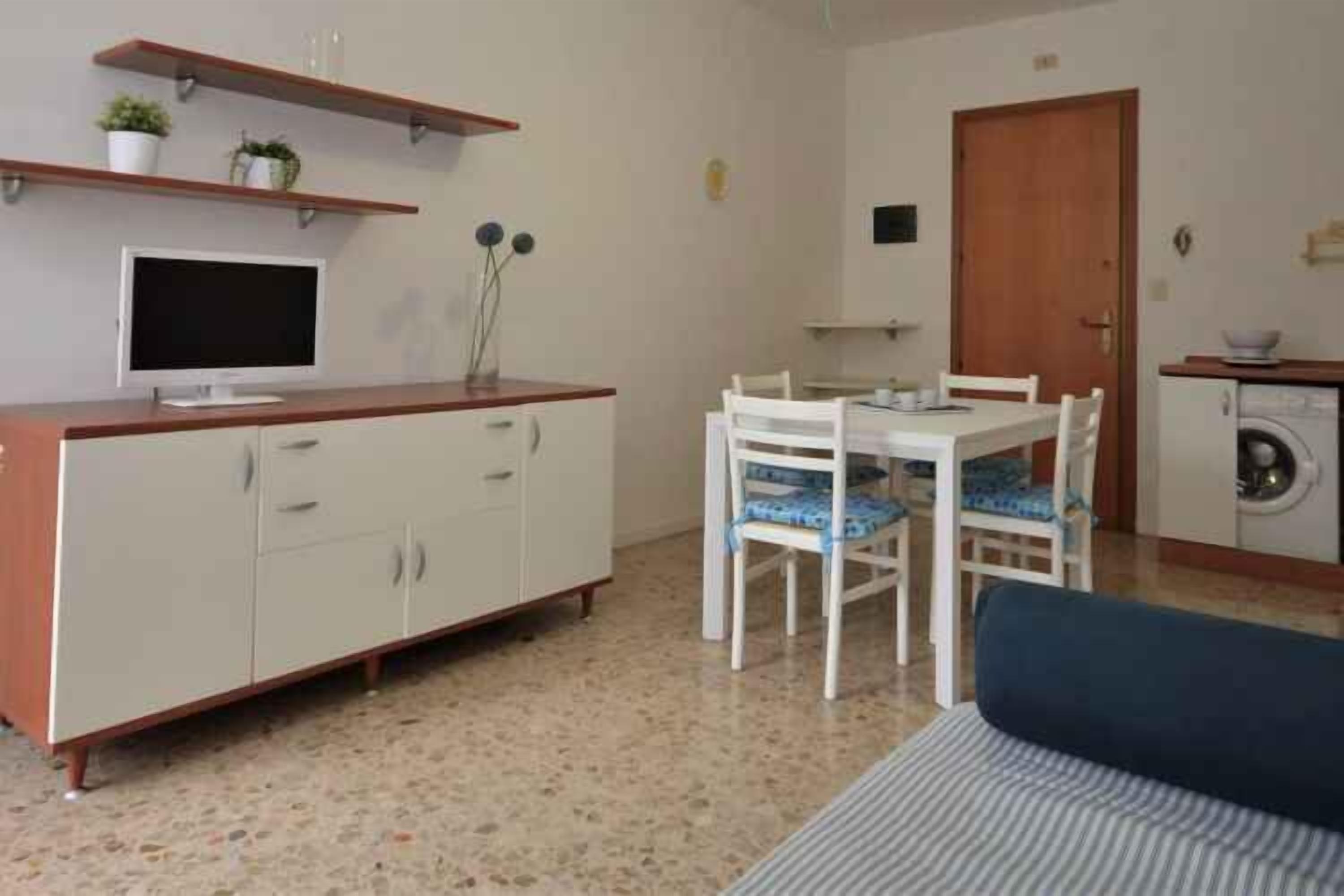 Un espace de vie compact comprenant un coin cuisine, un coin repas avec deux chaises, un canapé et un lave-linge.