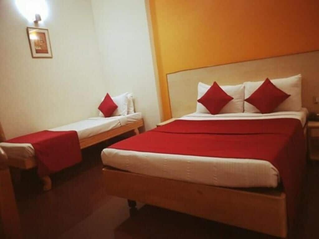 A hotel room with a large bed, two smaller beds, and red pillows.