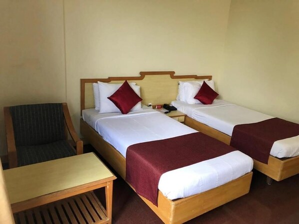 A hotel room with two single beds, a wooden nightstand, a chair, and a small table.