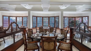 A dining area with a round table, wooden chairs, and large windows with decorative grills.
