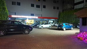 A parking area with several cars parked in front of a building with multiple windows and a red awning.