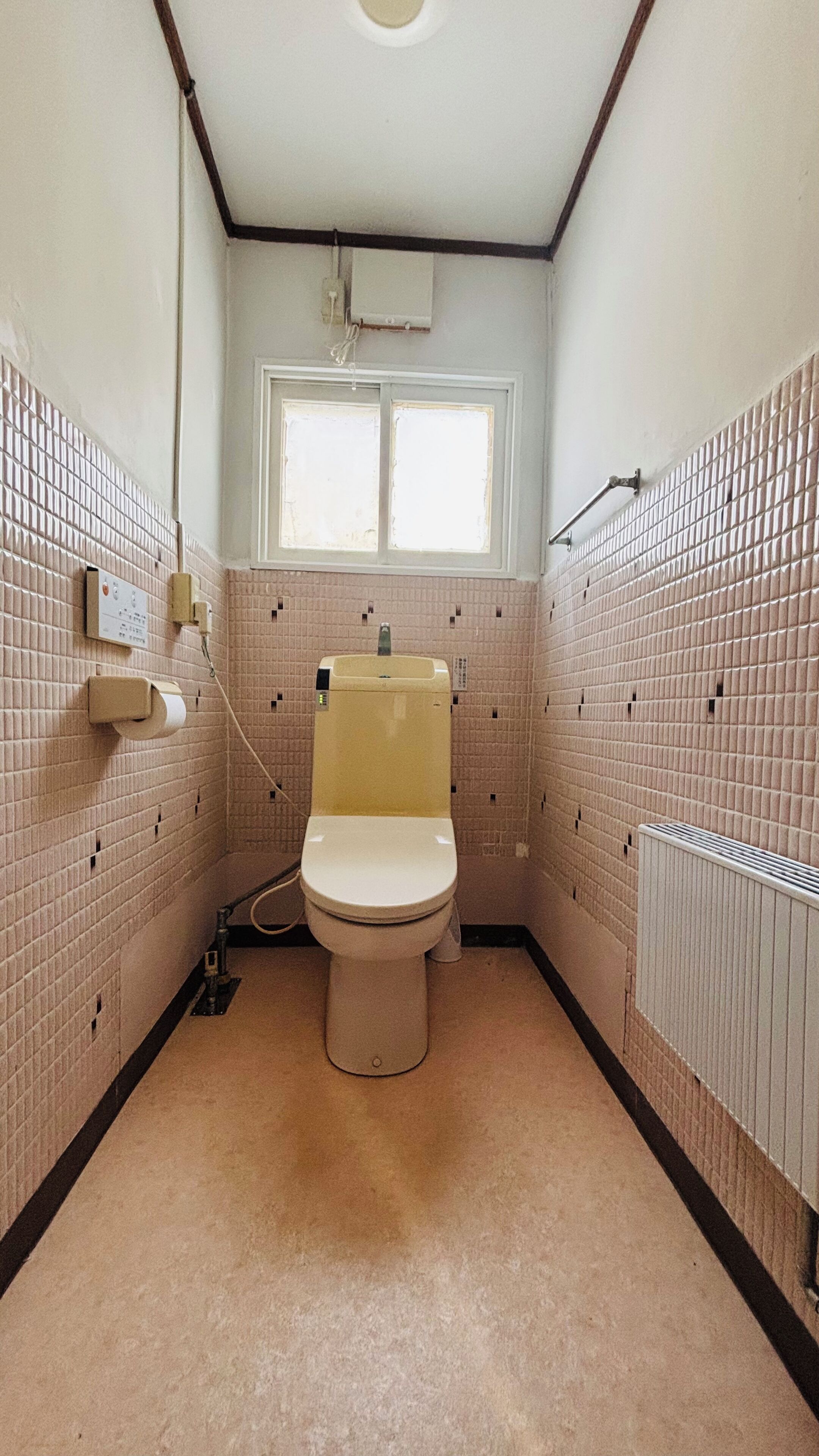 A small, tiled bathroom with a toilet, a window, and a radiator.