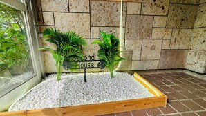 A planter box with white pebbles and two green plants, a sign reading "Second House," and a wooden wall in the background.
