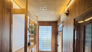 A hallway with wooden walls and a tiled floor, leading to a room with a large window and a door.