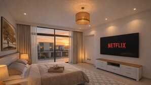 Ett modernt hotellrum med en stor säng, en platt-TV, en balkong med gardiner och utsikt över solnedgången.
