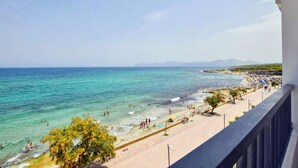 Una platja amb aigües turqueses cristal·lines, un passeig pavimentat i muntanyes a la distància.
