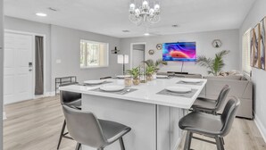 A modern kitchen with a central island, white cabinetry, and a large flat-screen TV. - Hot Tub, Fire Pit, Near the Beach! (Edgewater)