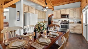 A dining area with a wooden table set for a meal, surrounded by light-colored cabinets and a ceiling fan. - Lofted Legacy Barn,  White Mountains AZ (Heber)