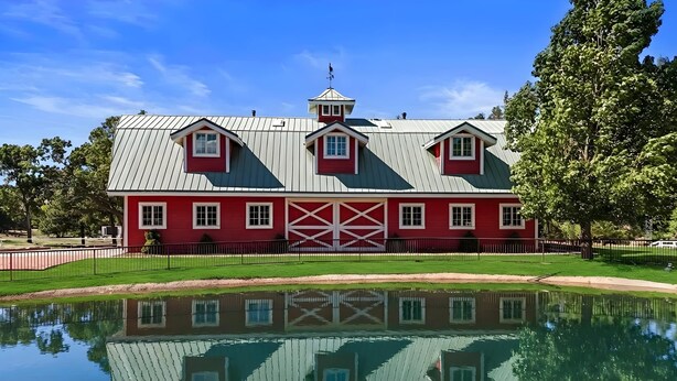 A red barn with a white roof and a small tower, surrounded by a fence and trees. - Lofted Legacy Barn,  White Mountains AZ (Heber)