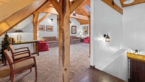 An attic room with exposed wooden beams, a high ceiling, and a skylight. There are two sofas, a red chair, and a small table with a lamp. - Lofted Legacy Barn,  White Mountains AZ (Heber)