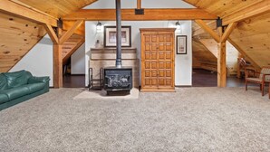 A cozy attic room with a wooden ceiling, a fireplace, a green sofa, and a wooden cabinet. - Lofted Legacy Barn,  White Mountains AZ (Heber)