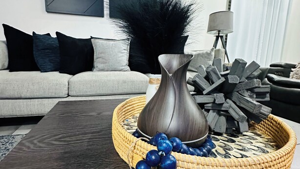 Ein modernes Wohnzimmer mit einem grauen Sofa, einem dunklen Couchtisch und einer dekorativen Ablage mit einer Vase und blauen Perlen.
