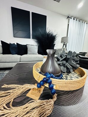 Un salon moderne avec un canapé gris, une table basse foncée et un plateau décoratif agrémenté d’un vase et de perles bleues.