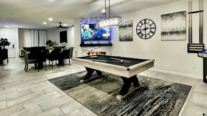 Ein modernes Wohnzimmer mit Billardtisch, Essbereich und Fernseher, der eine Sendung zeigt.