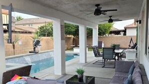Ein überdachter Außenbereich mit Pool, Sitzgelegenheiten und Deckenventilator.