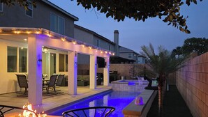 Ein modernes Haus mit Swimmingpool, Sitzgelegenheit im Freien und Lichterketten.
