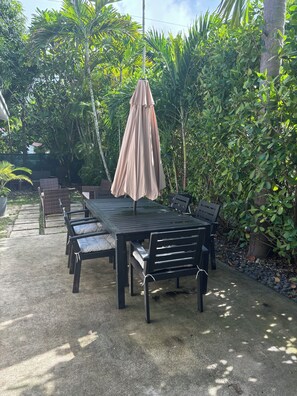 An outdoor patio with a table and chairs, surrounded by lush greenery and a hanging umbrella. - Palace at the Gables (Coral Gables)