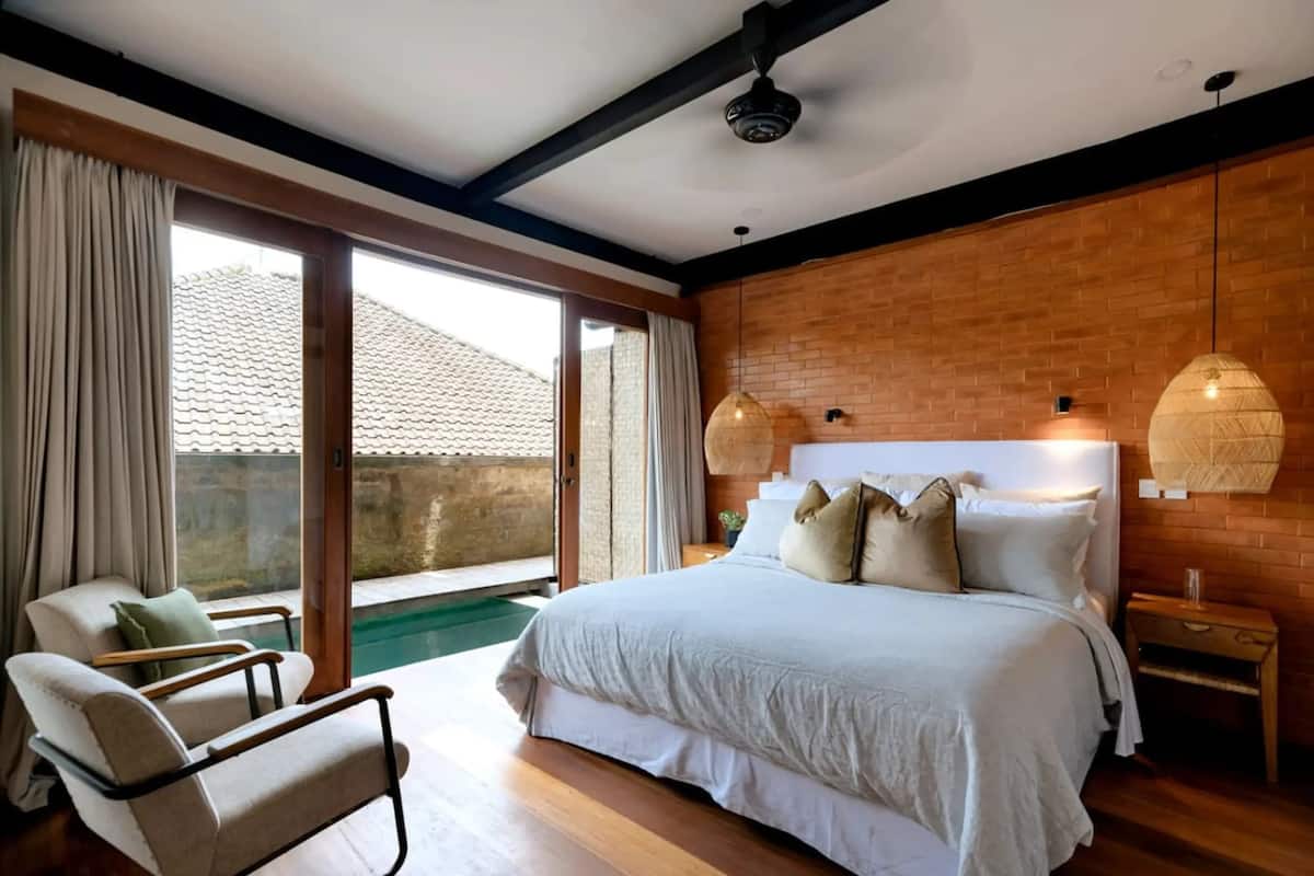 A bedroom with a large bed, a chair, a nightstand, and a view of a swimming pool.