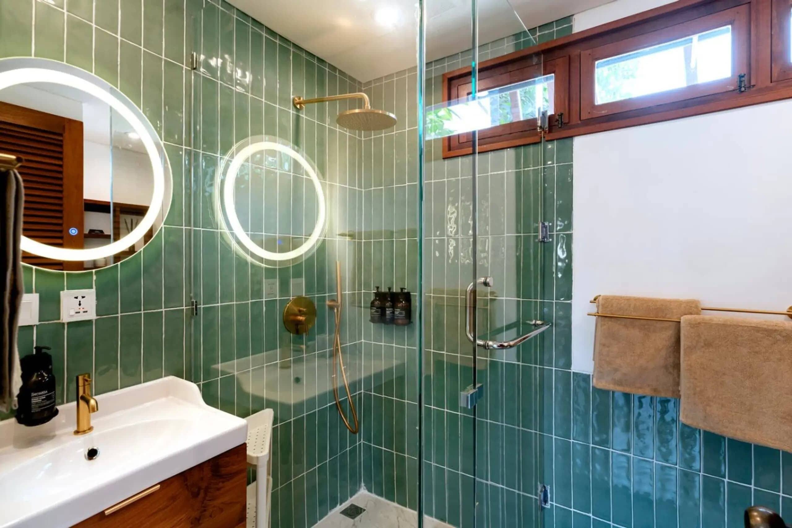 A bathroom with a glass-enclosed shower, a white sink, and a mirror with a ring light.